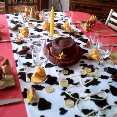 Ensemble composé d'une nappe imitation tissu rouge, d'un chemin de table en fausse fourrure, à imprimé vache et d'un centre de table en gâteau forme chapeau.