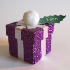 Boîte en forme de cadeau en carton violet scintillant, avec feuille de houx portant le prénom du convive en guise de chevalet.