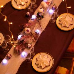 Table composée d'une nappe violette, d'un chemin de table imitation neige avec lumières, de serviettes blanches bordures violettes en forme d'étoile, de boîtes à bonbons violettes forme cadeaux et de centres de table en végétaux et figurines.